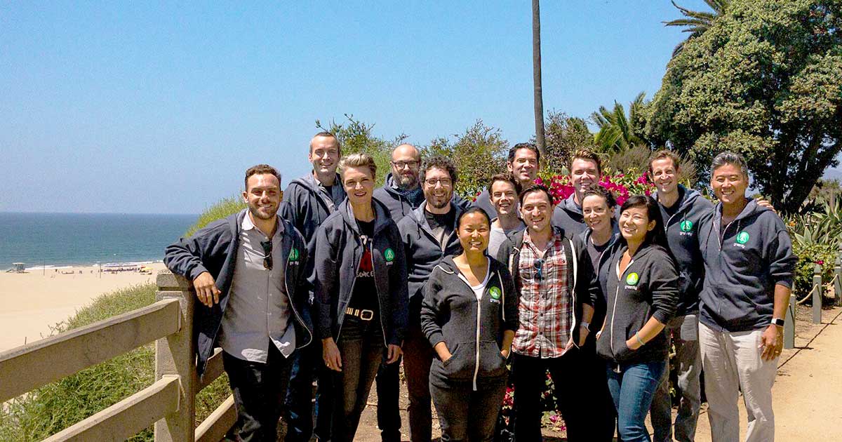 A photograph of the Greenfly HQ Team smiling and wearing branded hooded sweatshirts standing in front of the ocean in Santa Monica, CA