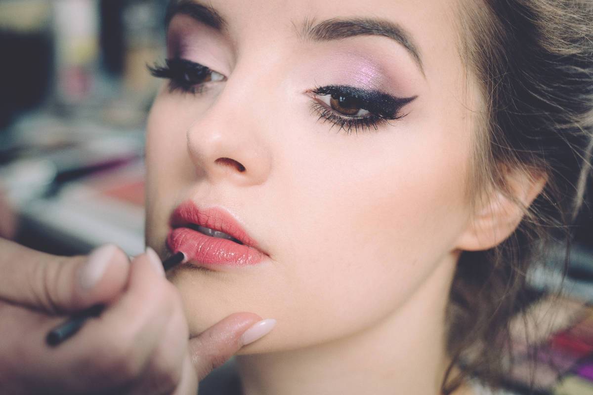 A photograph of a woman having lipstick applied to her lips.