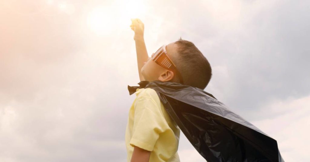 Boy dressed as superhero reaches up to sky, indicating powerful storytelling.
