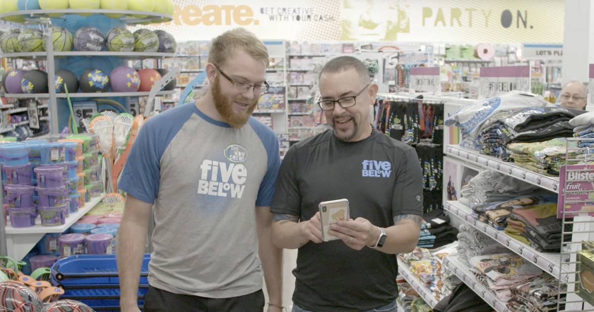 Two Five Below employees walk in store, looking at social on mobile phone.
