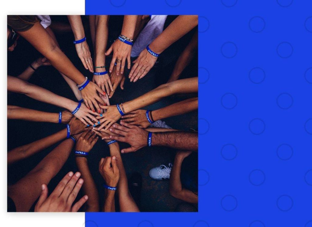 A photograph of over a dozen hands stacked in the middle before breaking a huddle.