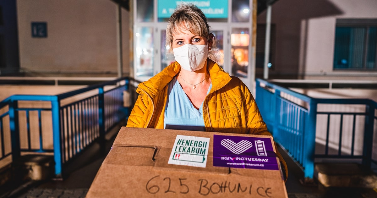 Female volunteer in mask carries box on GivingTuesday.