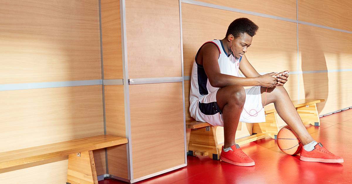Athlete with mobile phone on bench, demonstrating athletic department support for NIL