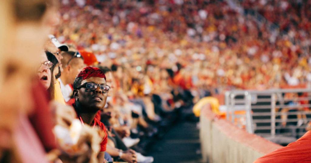 Crowd in stadium; male in foreground looking forward. Engage gen z sports fans.