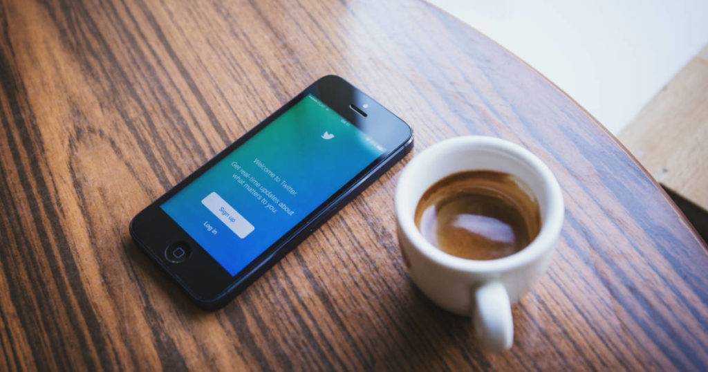 Twitter app on phone next to cup of coffee