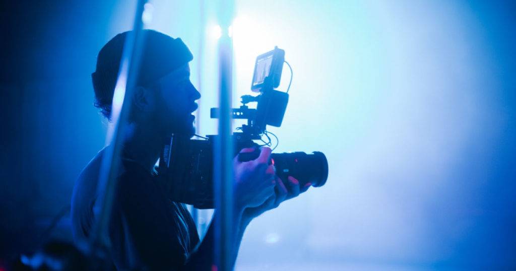 Man looking right and holding video camera to shoot digital asset.