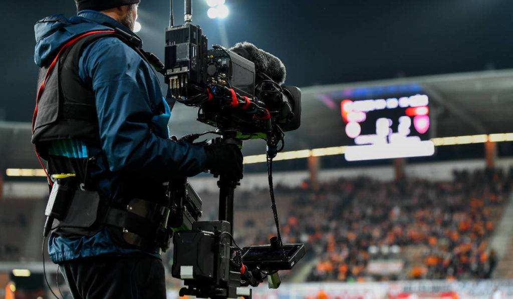 Cameraman behind playing field during soccer match, video stored in digital asset management system