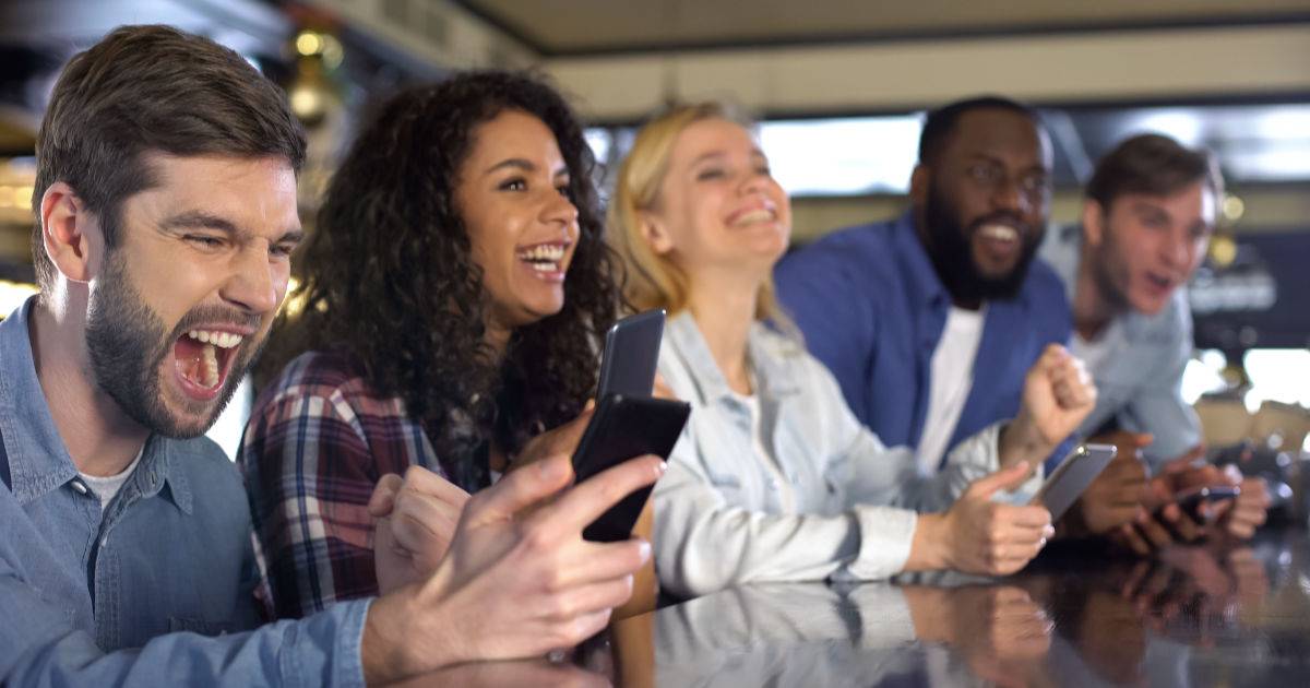 sports apps being used by 5 male and female fans sitting in a bar.