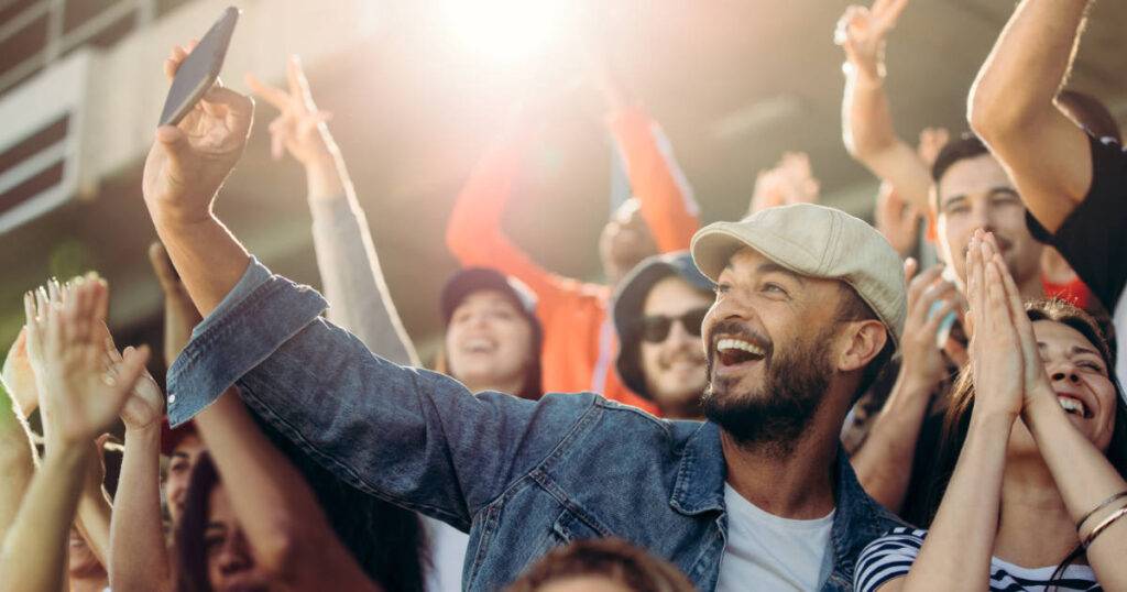 Cheering fan taking selfie in stadium crowd showcasing global fan engagement in sports.